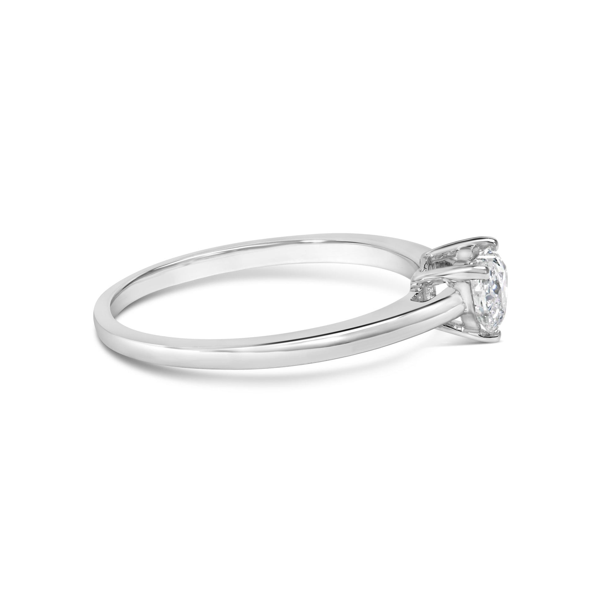 Side angle of a white metal ring with a single heart-shaped white gemstone in a three-prong setting.
