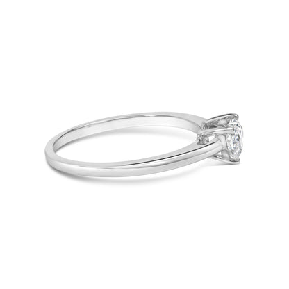 Side angle of a white metal ring with a single heart-shaped white gemstone in a three-prong setting.