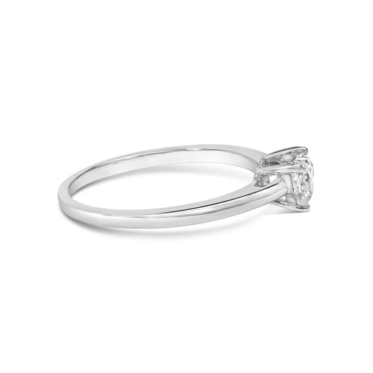 Side angle of a white metal ring with a single heart-shaped white gemstone in a three-prong setting.