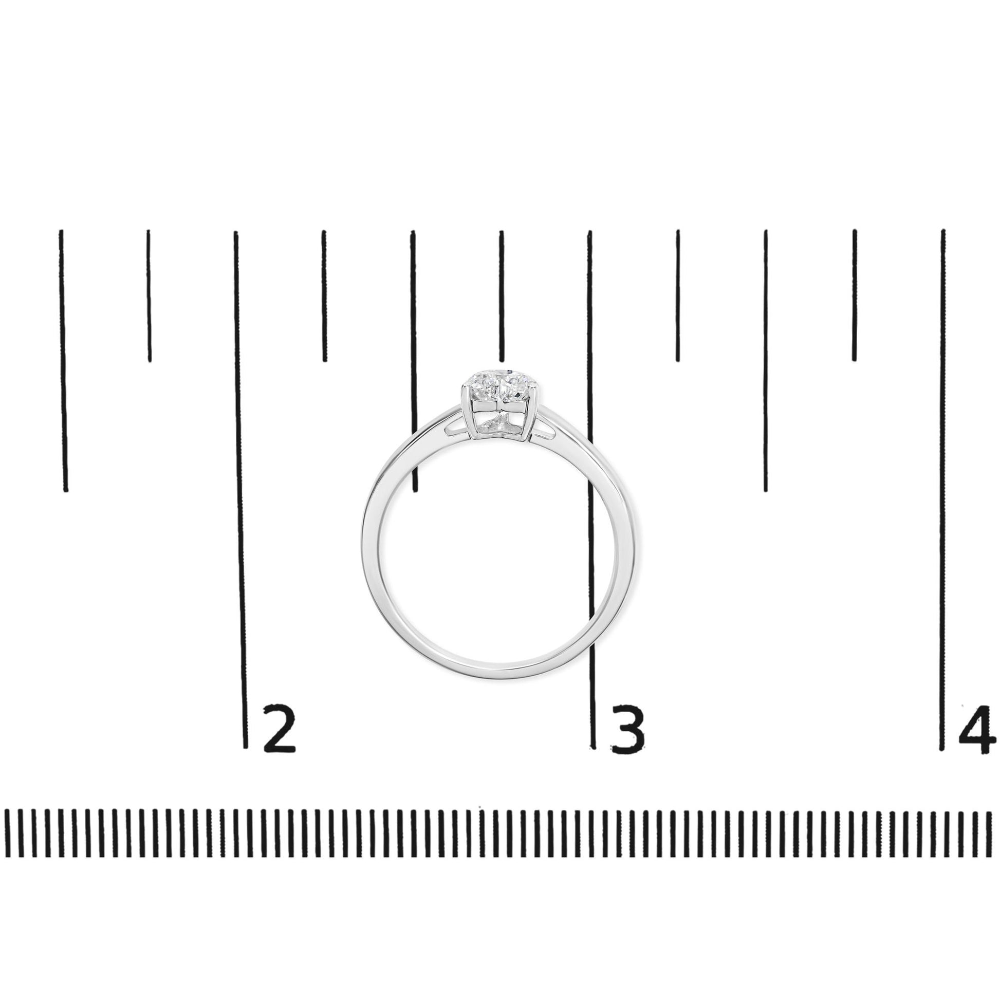 Top view of a white metal ring with one heart-shaped white gemstone in a three-prong setting, placed on a ruler for size reference.