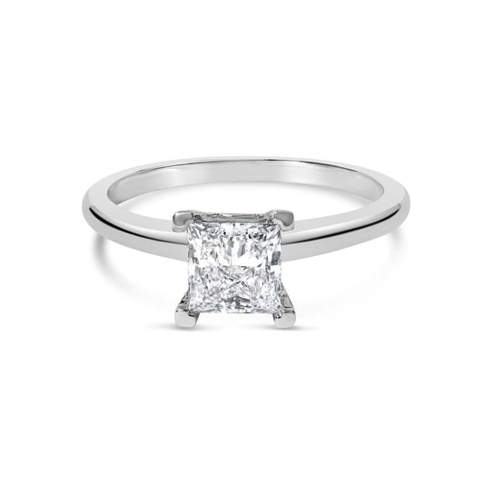 Front view of a white metal ring with a single princess shape white gemstone in a prong setting.