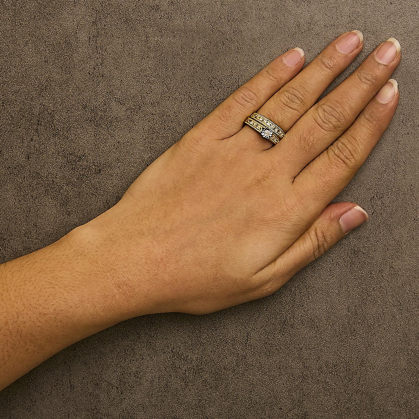 Yellow metal ring with a central white gemstone and additional white gemstones in prong settings, worn on a model's finger, shot from above.