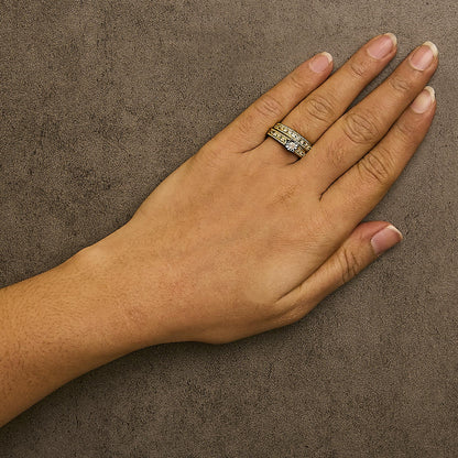 Yellow metal ring with a central white gemstone and additional white gemstones in prong settings, worn on a model's finger, shot from above.