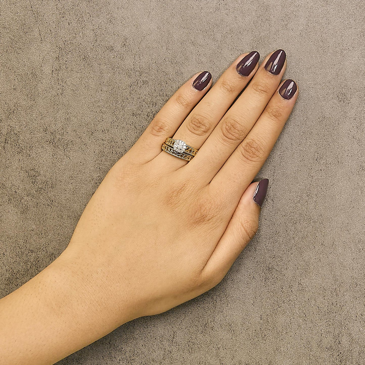 Yellow metal ring with one round white gemstone in a 4-prong setting and multiple smaller round white gemstones in prong settings, worn on a model's hand, top-down angle.