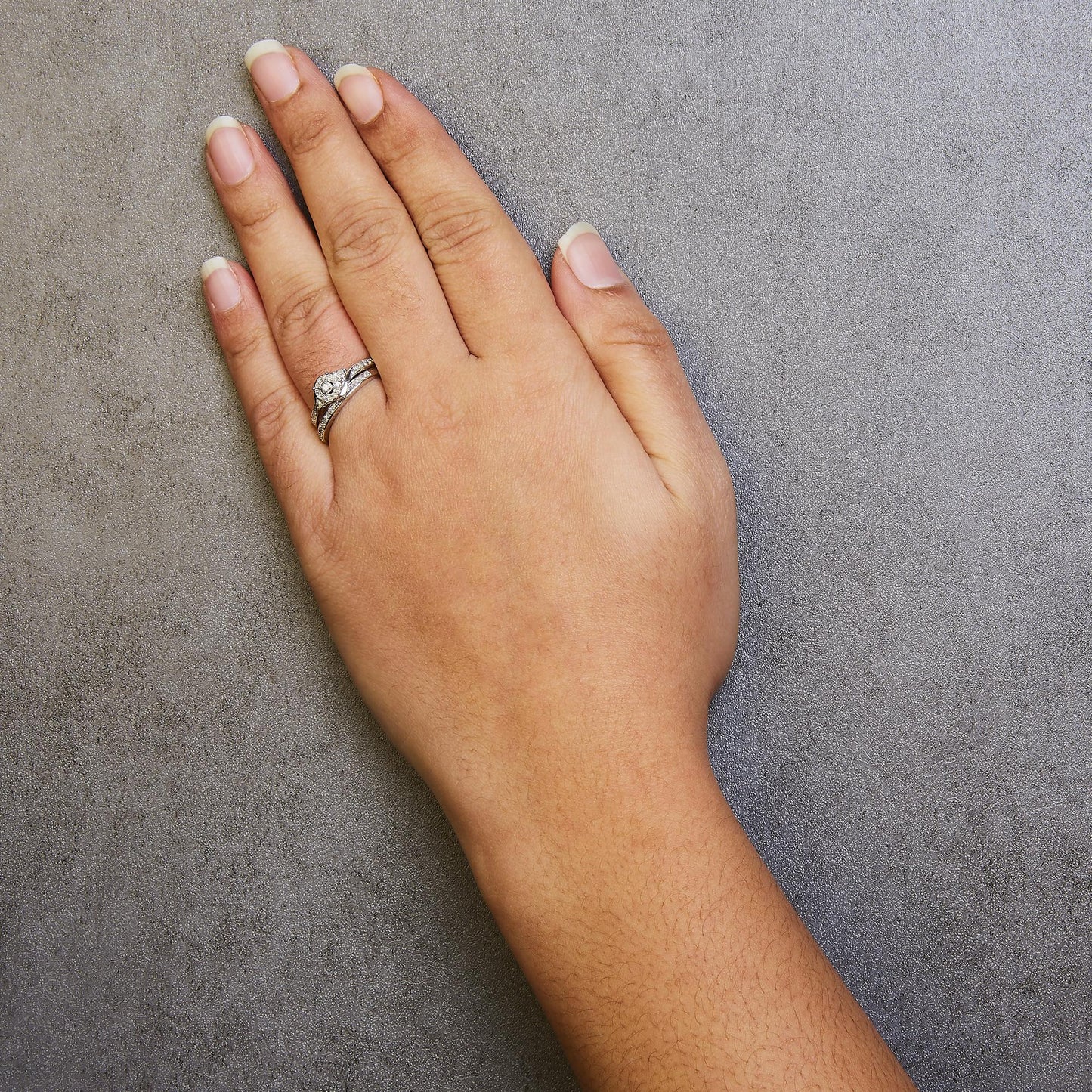 Close-up top view of a hand wearing two white metal rings featuring multiple round prong-set white gemstones.