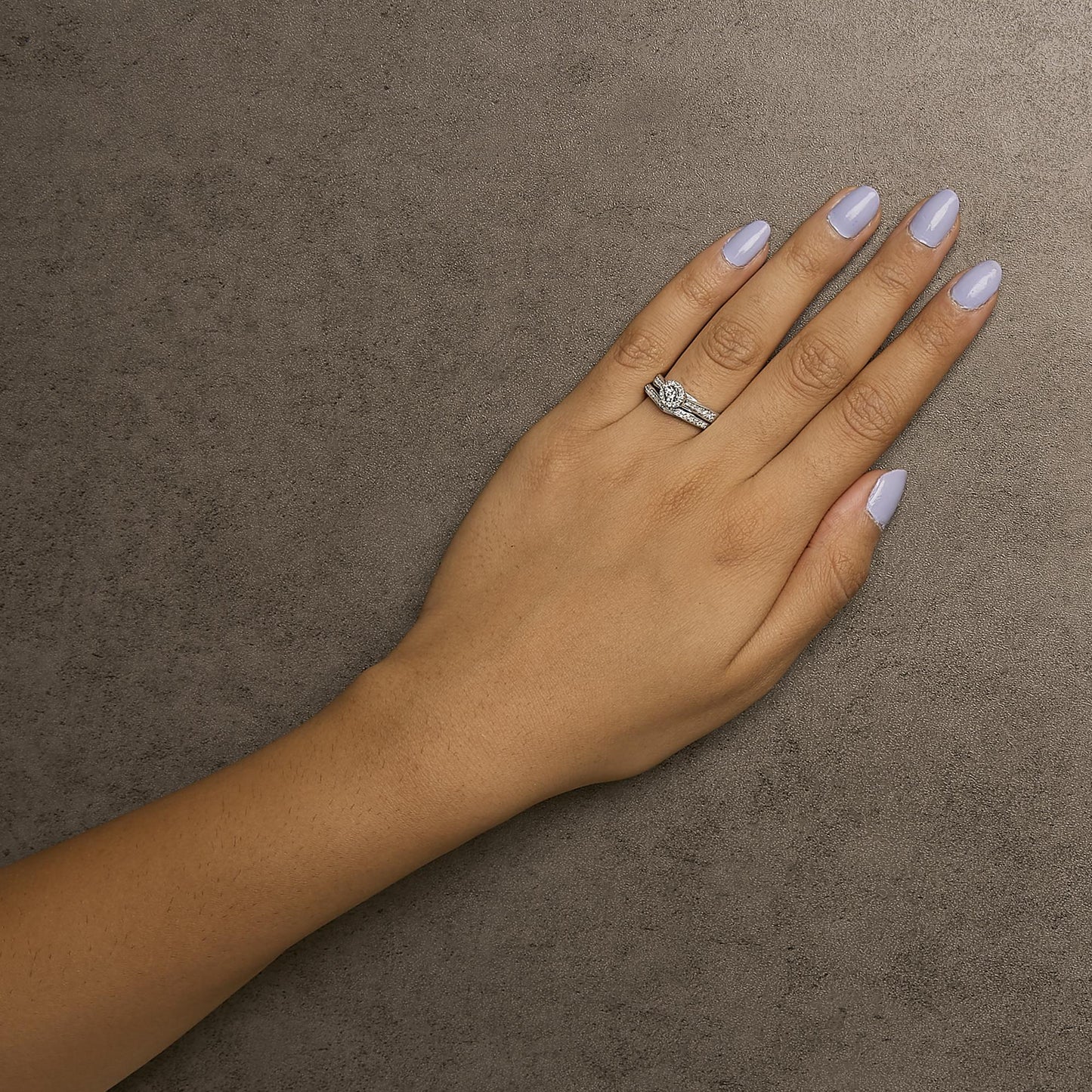 White metal ring with multiple round white gemstones in prong settings, worn on a model's hand, top-down angle.