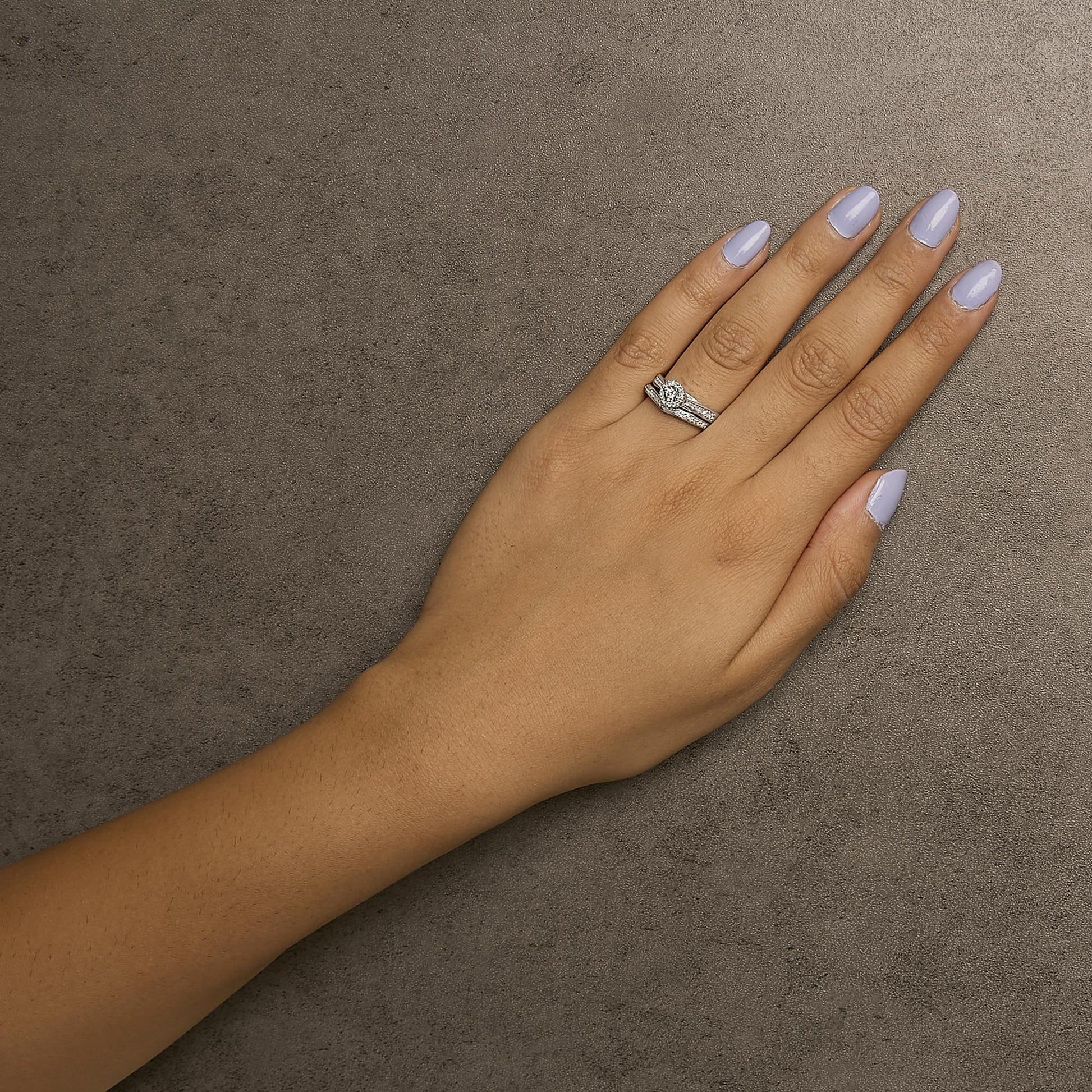 White metal ring with multiple round white gemstones in prong settings, worn on a model's hand, top-down angle.
