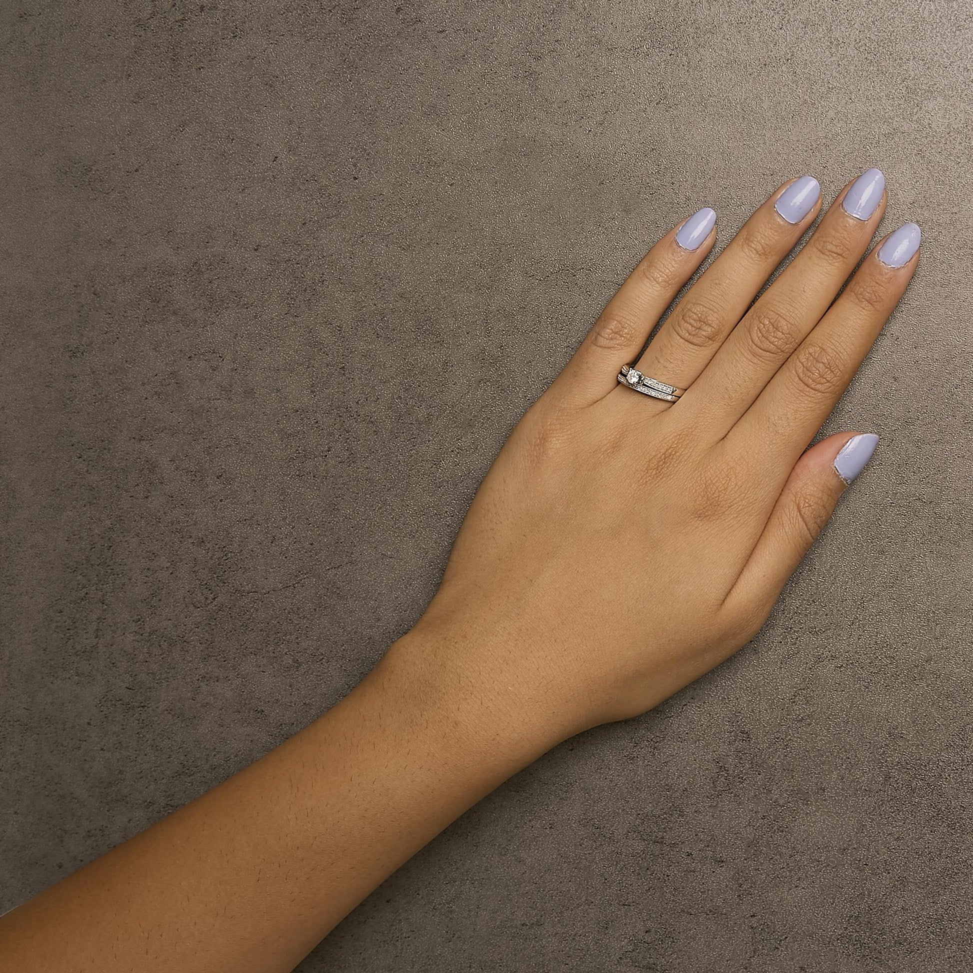 Top-down angled view of a white metal ring set on a model's finger featuring one round gemstone in a four-prong setting and multiple round gemstones in shared prong settings.