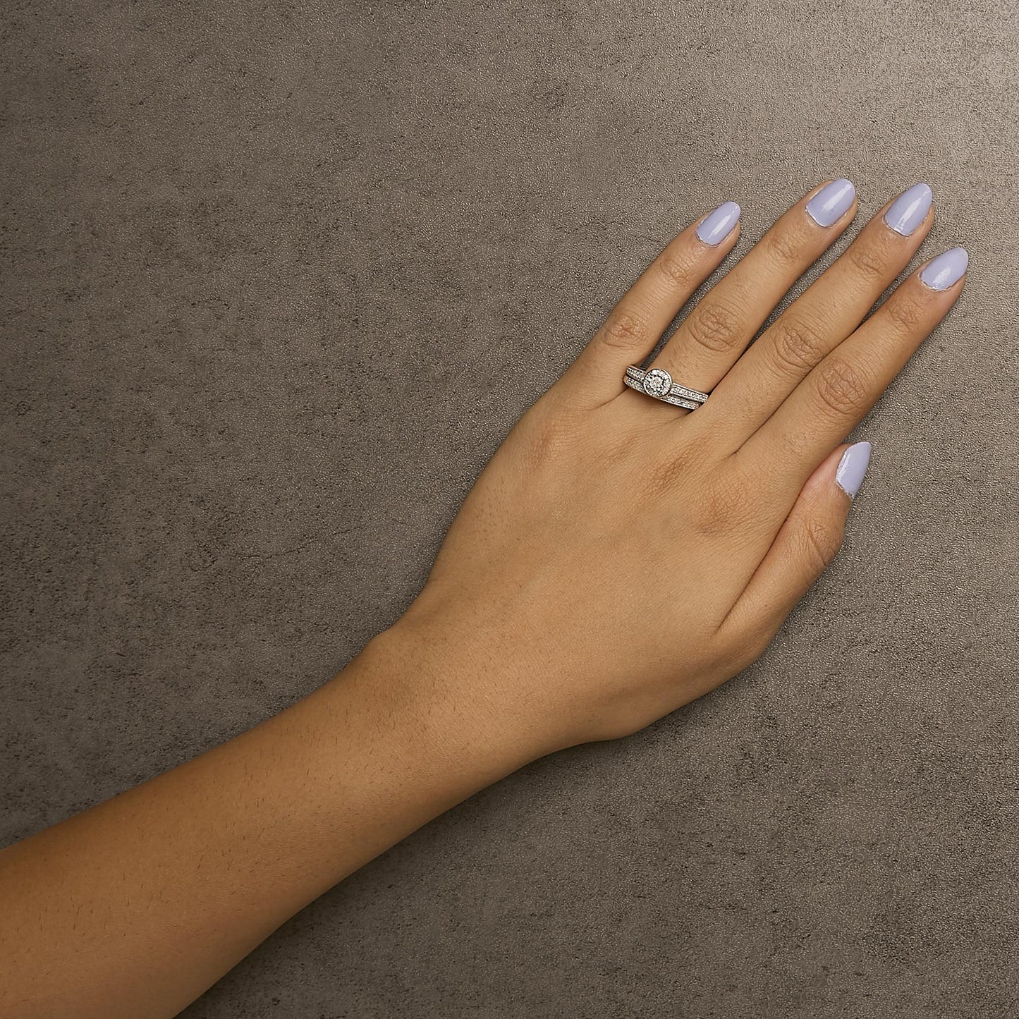 White metal ring with a round white gemstone in the center and multiple smaller white gemstones in pave settings, shown on a model's hand from a top angle.