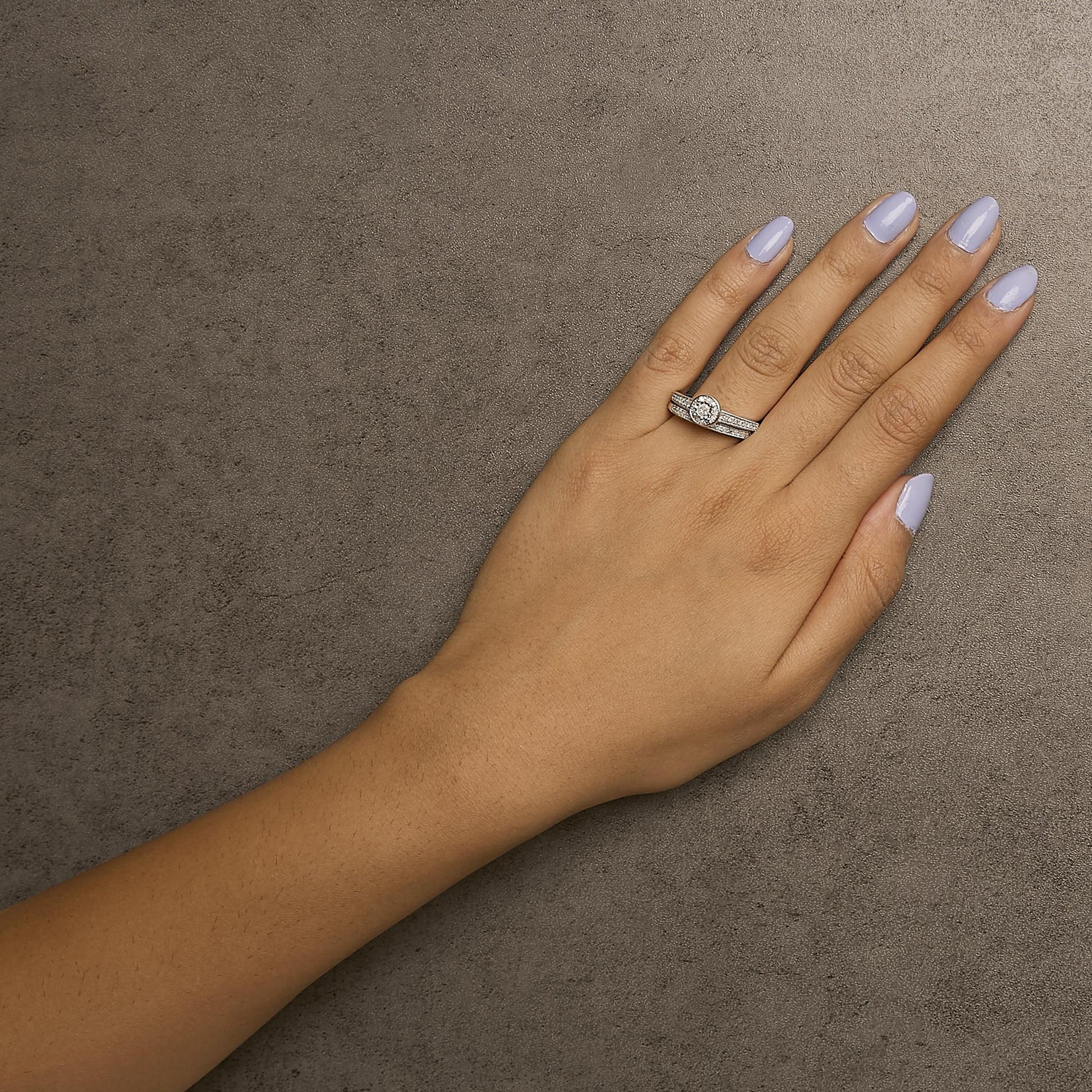 White metal ring with a round white gemstone in the center and multiple smaller white gemstones in pave settings, shown on a model's hand from a top angle.