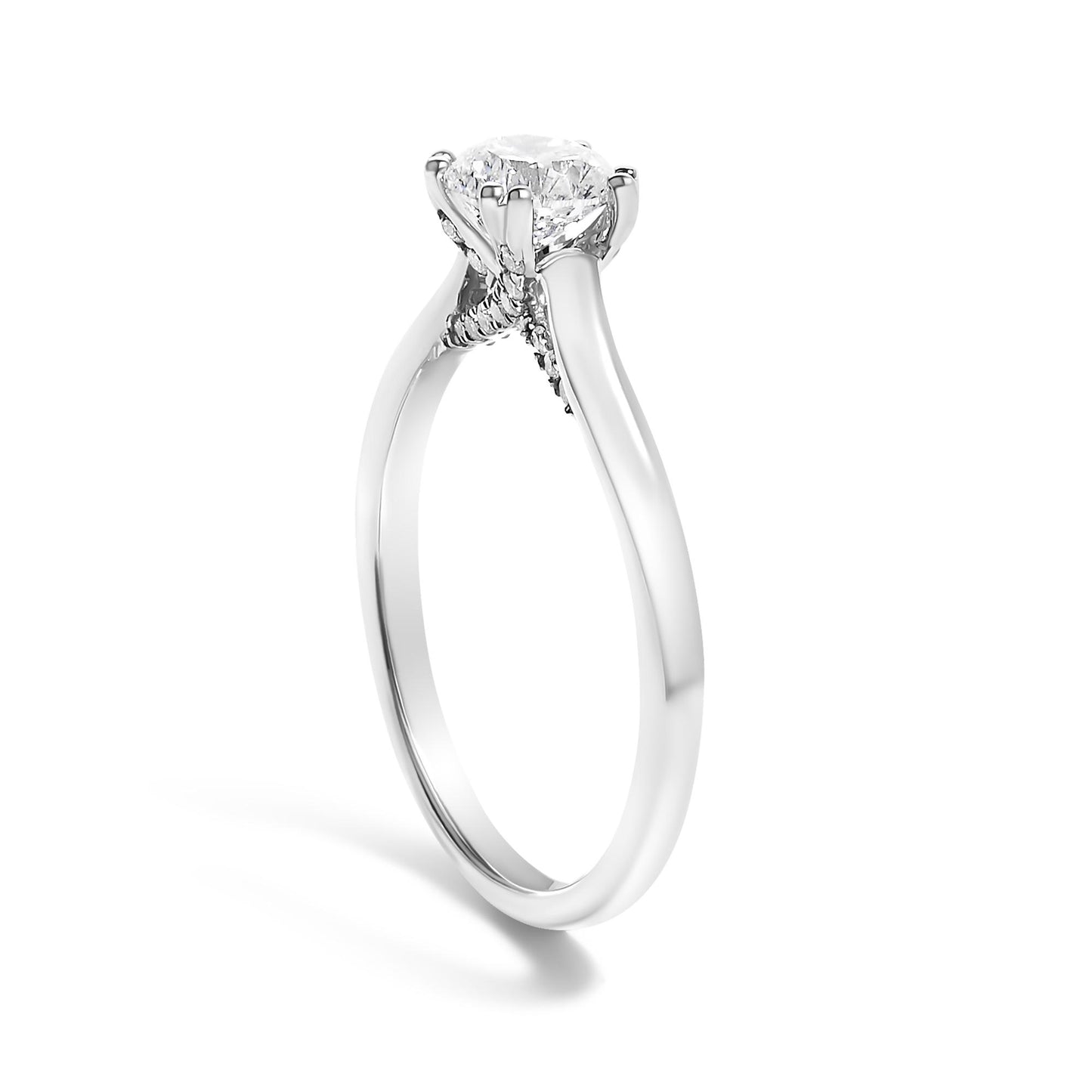 White metal ring viewed at an angle, featuring one round white gemstone in a four-prong setting and multiple smaller round white gemstones in prong settings along the band.