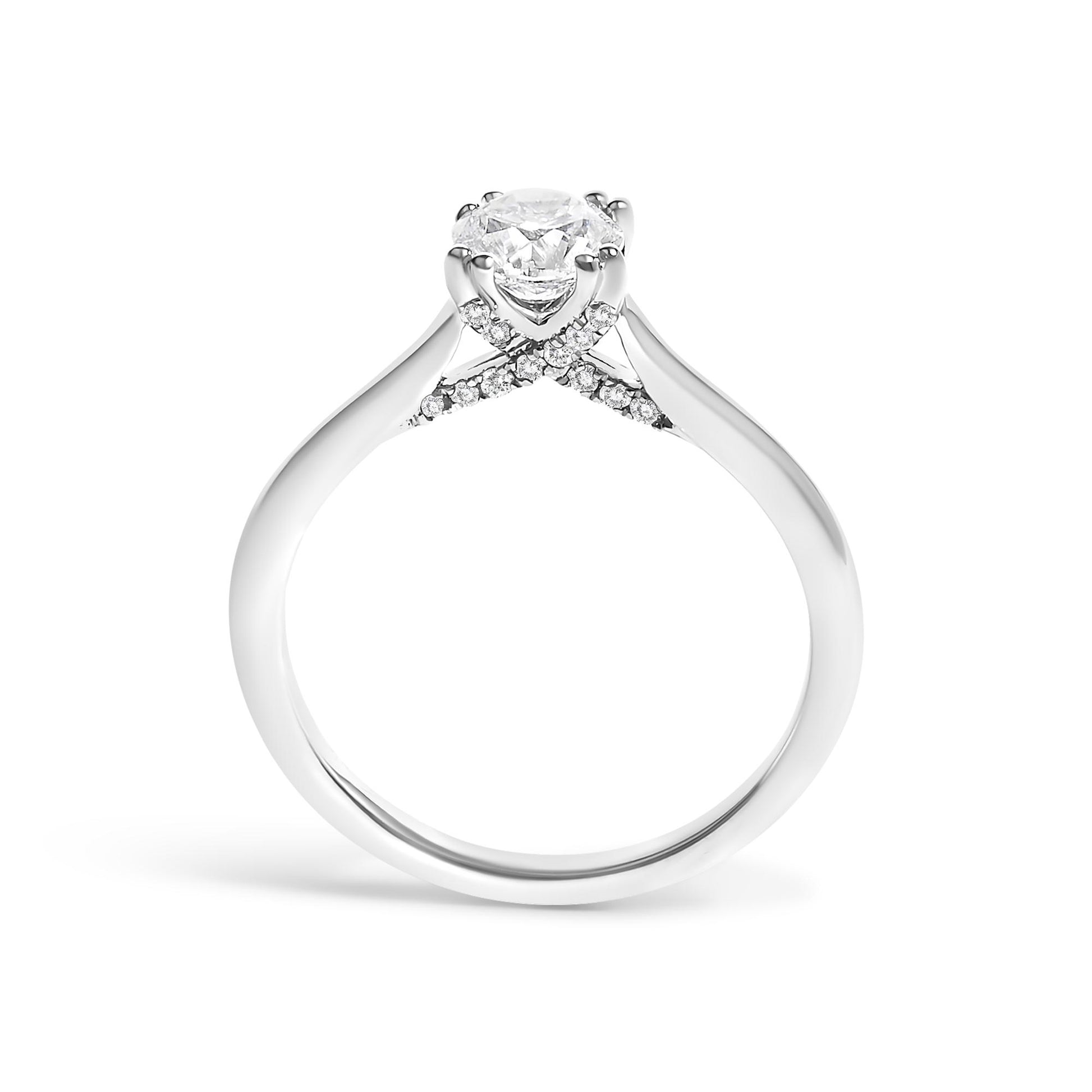 White metal ring shown from the side with a round white gemstone in a 4-prong setting and multiple smaller round white gemstones on a crossing band.