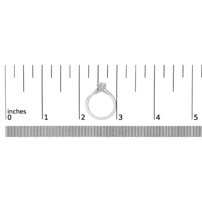 White metal ring with a single round white gemstone in a four-prong setting and multiple smaller round white gemstones in prong settings, shown from the side on a ruler for size reference.