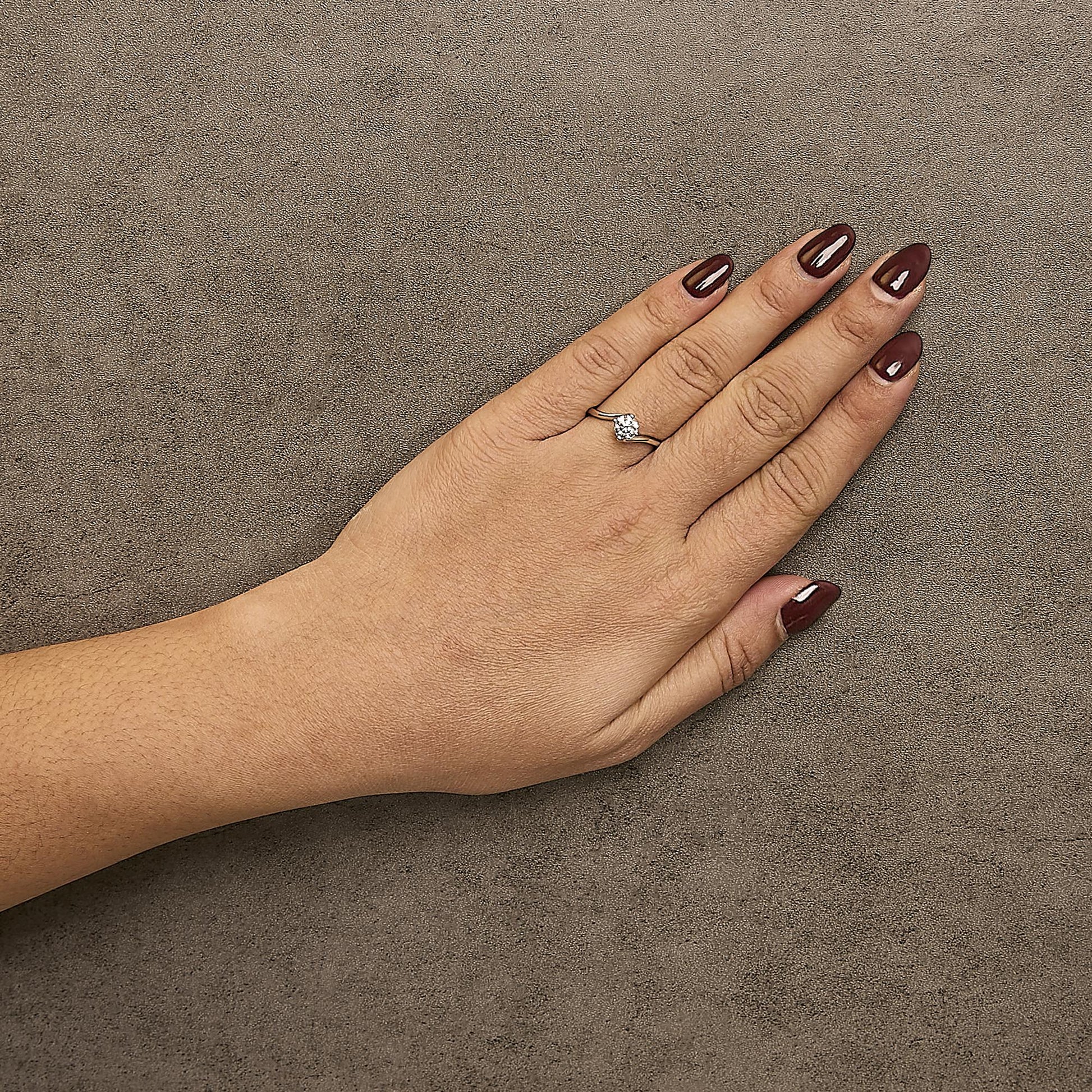 White metal ring with a round white gemstone in a four-prong setting surrounded by smaller round white gemstones in prong settings, worn on a model's hand, shot from above at an angle.