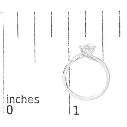 White metal ring with one round white gemstone in a 4-prong setting and multiple smaller round white gemstones in prong settings along the band, shown from a side angle on a ruler for size reference.