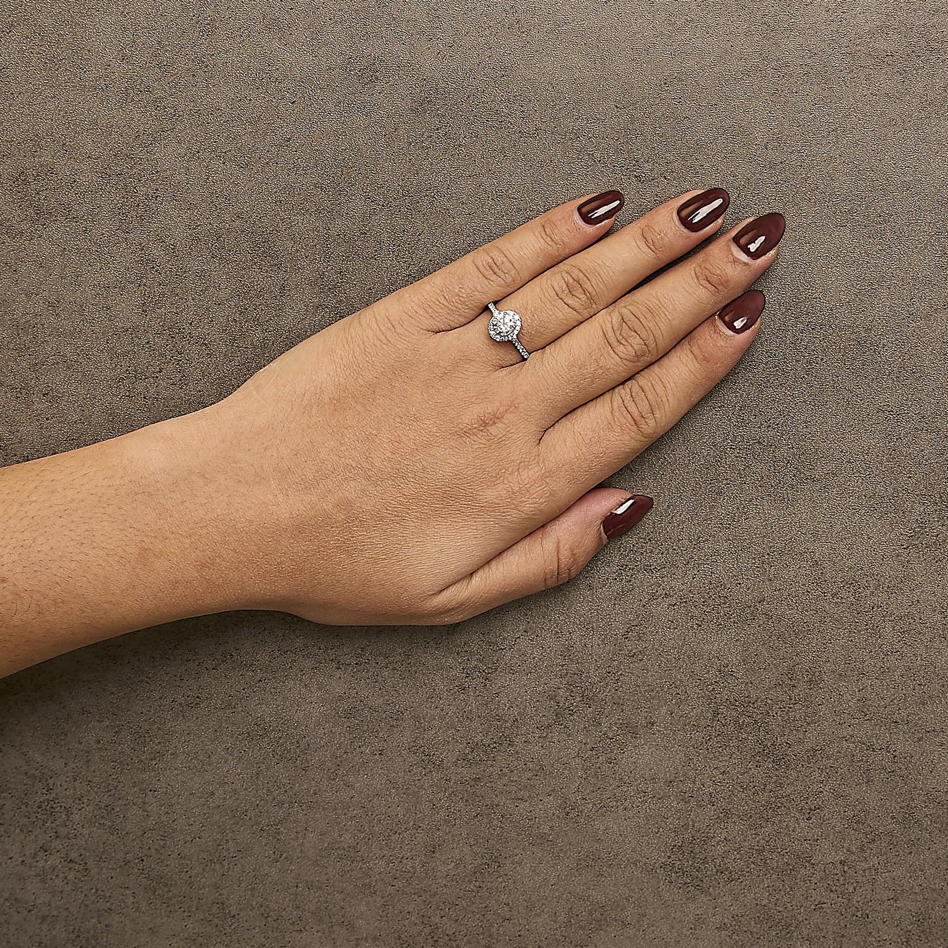 Top view of a white ring on a model’s finger, featuring a round center gemstone with a four-prong setting, surrounded by multiple smaller white gemstones in micro-pave settings along the band.