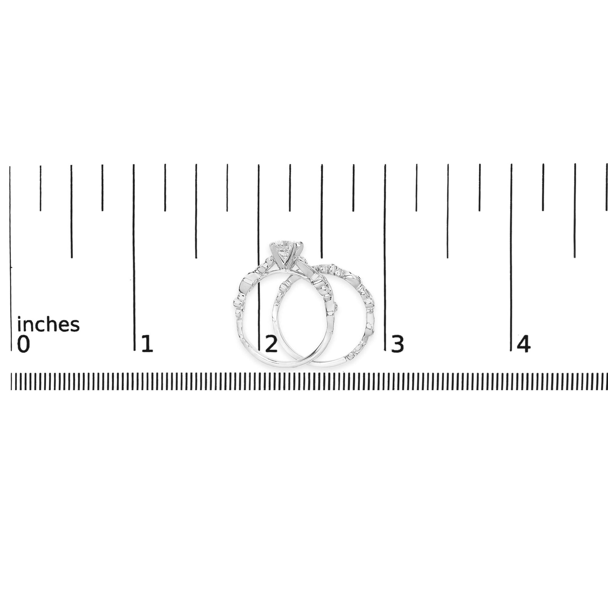 Two white metal rings with round white gemstones in prong settings, shown on a ruler scale from a front angle.