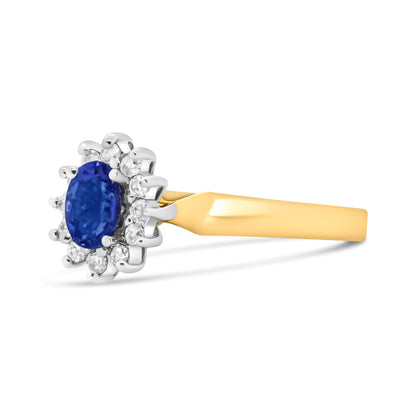Yellow metal ring with an oval blue gemstone surrounded by round white gemstones in prong settings, shown in a side view angle.