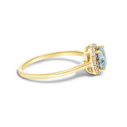 Side angle view of a yellow metal ring featuring a round blue gemstone in a four-prong setting, surrounded by a halo of round white gemstones in a shared prong setting.