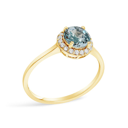 Yellow metal ring with a round blue gemstone in a four-prong setting, surrounded by a halo of round white gemstones in a shared prong setting, shown in a close-up angled view.