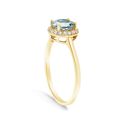 Yellow ring shown at an angle with a round blue gemstone in a four-prong setting at the center, surrounded by a halo of round white gemstones in shared prong settings.