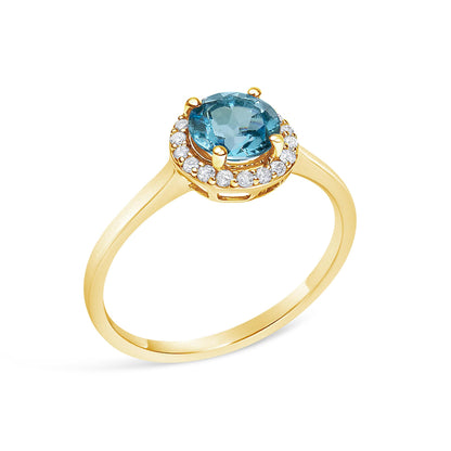 Yellow metal ring with a round blue gemstone in a four-prong setting, surrounded by round white gemstones in a shared prong setting, shown from a slightly angled top view.