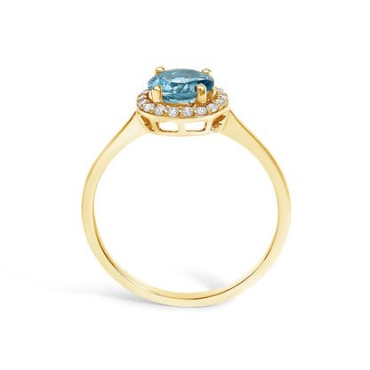 Ring with a yellow-colored band shown from the side angle, featuring a round blue gemstone in a four-prong setting surrounded by a halo of round white gemstones in a shared prong setting.