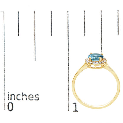 Yellow metal ring with a round blue gemstone center set in four prongs, surrounded by a halo of round white gemstones in a shared prong setting, shown on a scale with an inch ruler, side profile view.