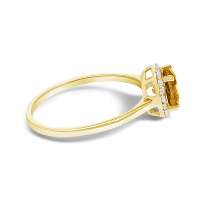 Side angle view of a yellow ring with a central round orange gemstone in a four-prong setting, surrounded by multiple small round white gemstones in a shared prong setting.