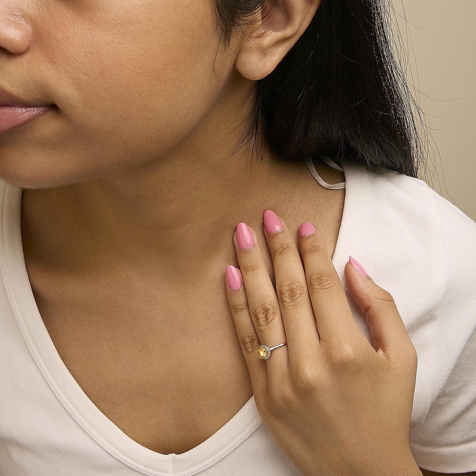 Yellow metal ring with a round orange gemstone in a four-prong setting, surrounded by a circle of small round white gemstones in shared prong settings, shown worn on a model's hand from a front angle.