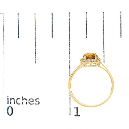 Yellow metal ring with a round orange gemstone in a four-prong setting surrounded by small white gemstones in a shared prong setting, shown on a scale from a side angle.