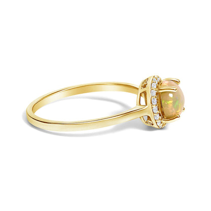 Side angle view of a yellow metal ring with a round multi-color opal gemstone held by four prongs, surrounded by a shared prong setting of round white gemstones.