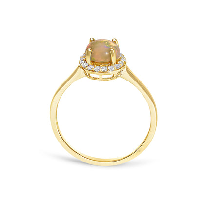 Yellow metal ring with a round multicolor opal gemstone in a four-prong setting, surrounded by a halo of round white gemstones in shared prong settings, shown from the side angle on a white background.