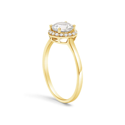 Yellow metal ring shown in a side angle with a round white gemstone set in a four-prong setting, surrounded by a halo of small round white gemstones in shared prong settings.