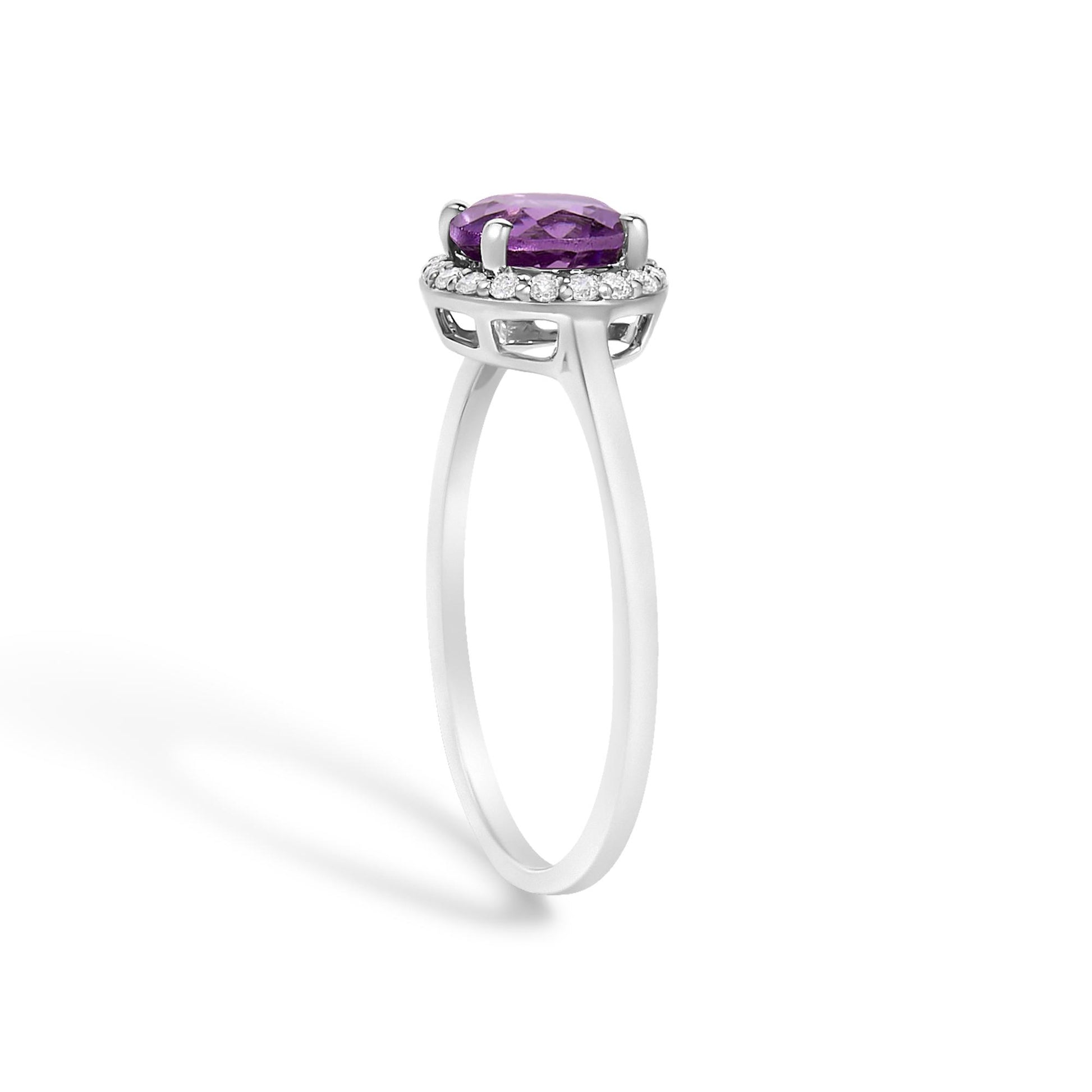 Side angle view of a white metal ring featuring a round purple gemstone in a four-prong setting, surrounded by a halo of round white gemstones in shared prong settings.