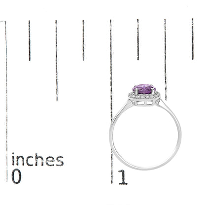 White metal ring with a round purple gemstone in a four-prong setting, surrounded by a halo of small white round gemstones in shared prong settings, shown on a scale from a side angle.