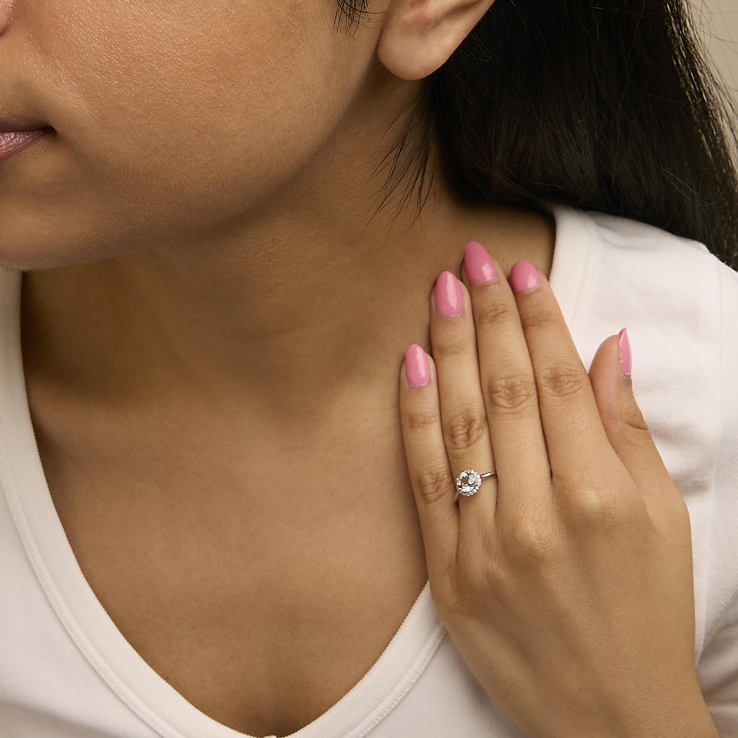 Close-up angled view of a white metal ring with a round blue gemstone center surrounded by multiple round white gemstones in shared prong settings, worn on a model's finger.