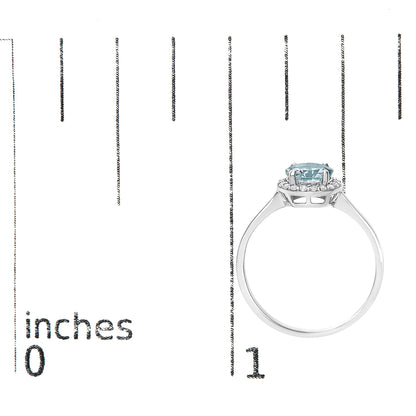 White metal ring with a round blue gemstone in a four-prong setting, surrounded by round white gemstones in a shared prong setting, shown from the side on a scale.