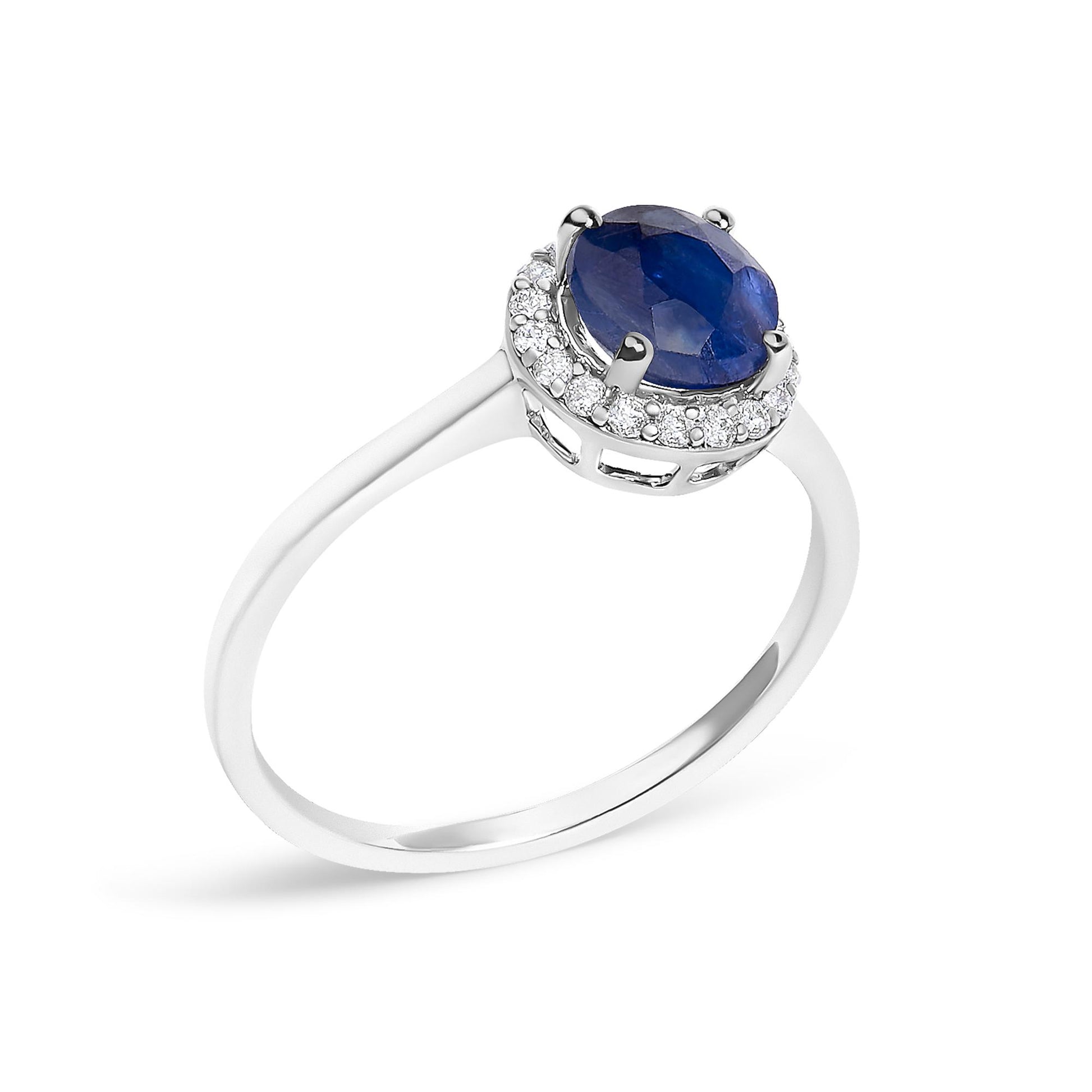 Close-up angle of a white metal ring with a round blue gemstone center set in a four-prong setting, surrounded by a halo of round white gemstones in a shared prong setting.
