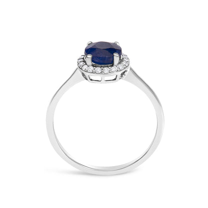 White ring shown from side angle with a round blue gemstone held by four prongs in the center and a halo of small round white gemstones in shared prong setting surrounding it.