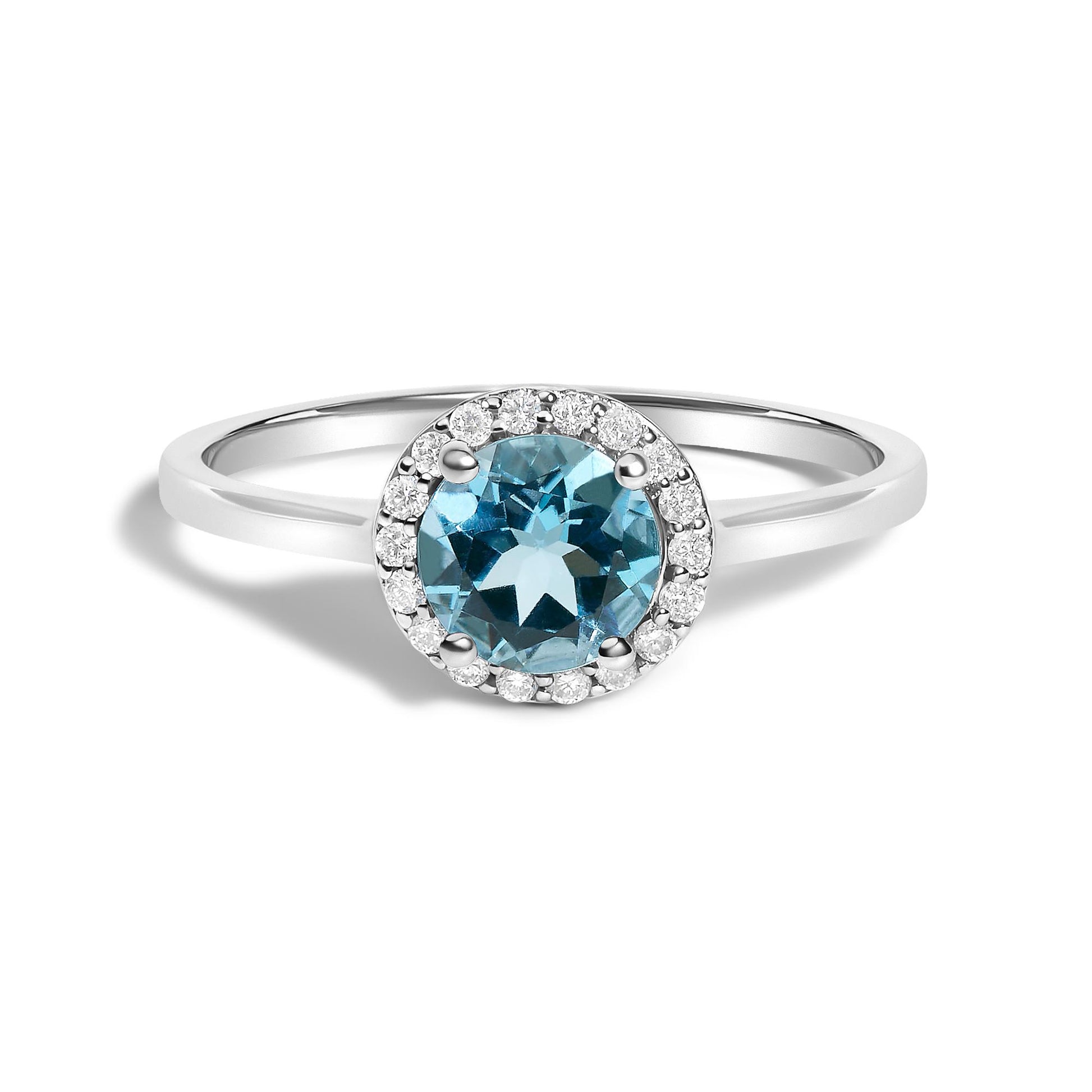 White metal ring with a round blue gemstone center held by four prongs, surrounded by a halo of small round white gemstones in shared prong setting, shown from a front angle on a white background.