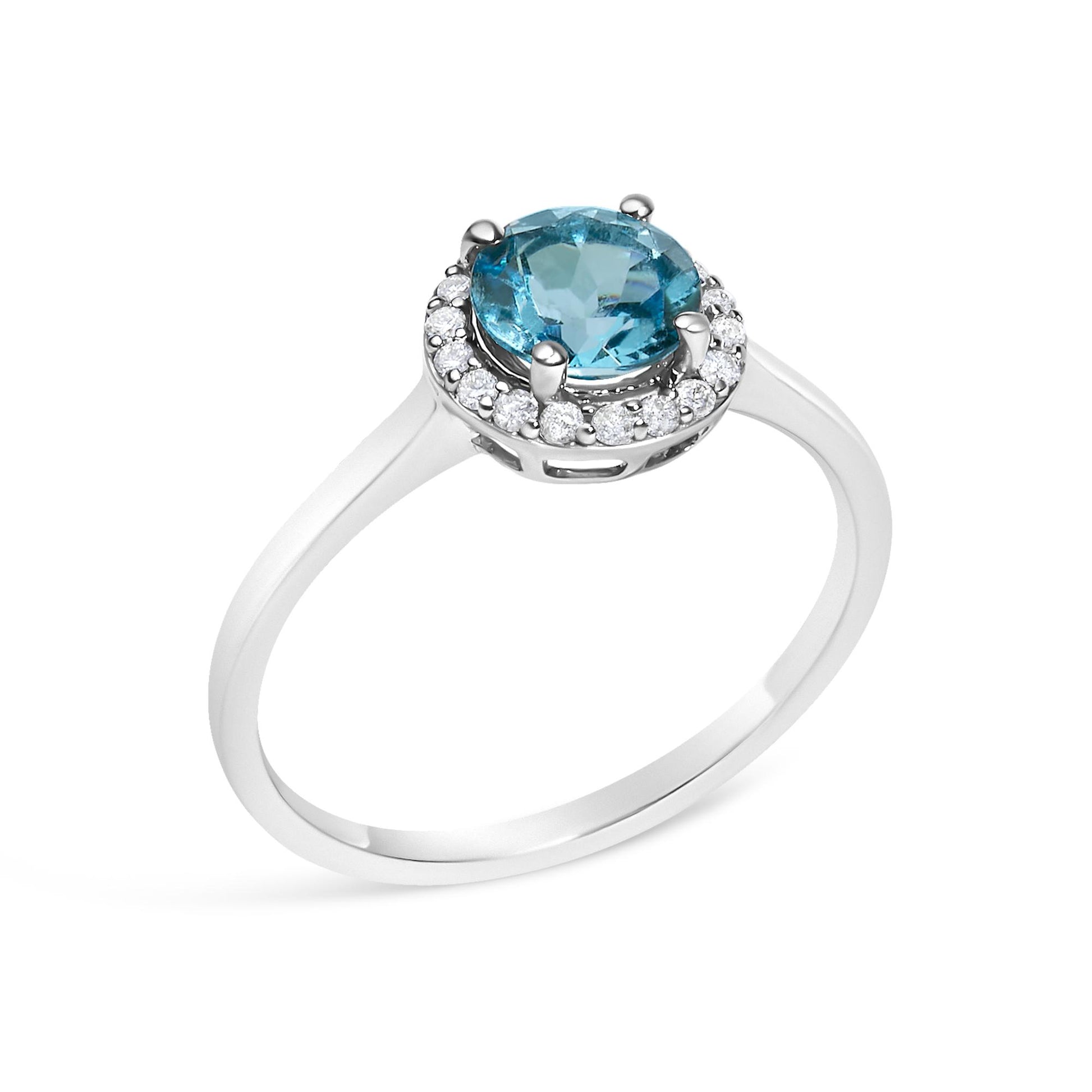 White metal ring with a round blue gemstone center set in a four-prong setting, surrounded by a halo of round white gemstones in shared prong setting, shown at an angled top view.