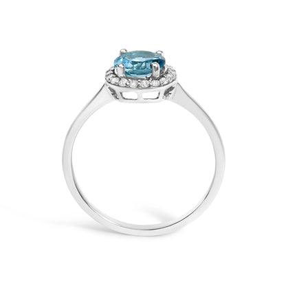 White ring with a round blue gemstone in a four-prong setting, surrounded by small round white gemstones in a shared prong setting, shown from the front angle.