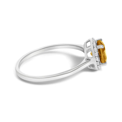 Close-up side angle of a white metal ring featuring a round orange gemstone held by a four-prong setting, surrounded by multiple small round white gemstones in a shared prong setting.