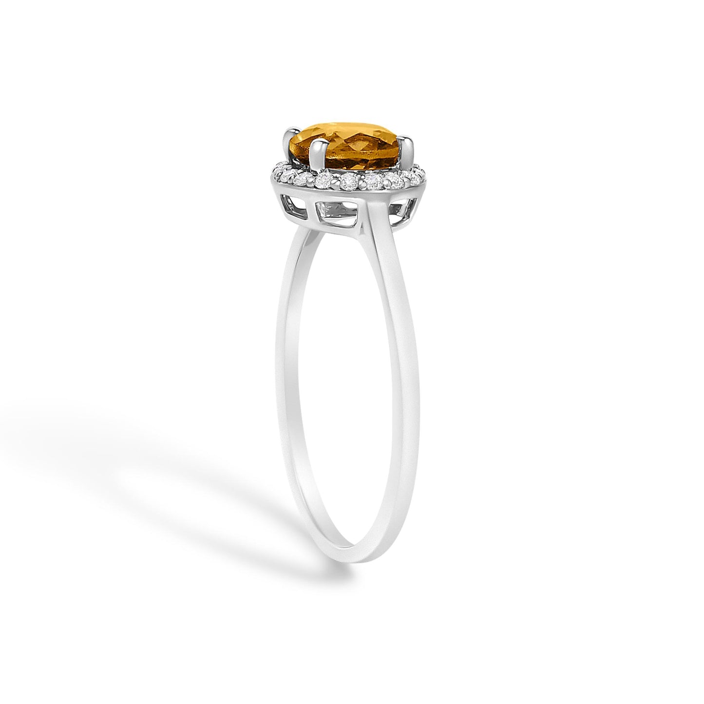 Side view of a white metal ring featuring a round orange gemstone in a four-prong setting surrounded by a halo of small round white gemstones in shared prong settings, shown on a white background.