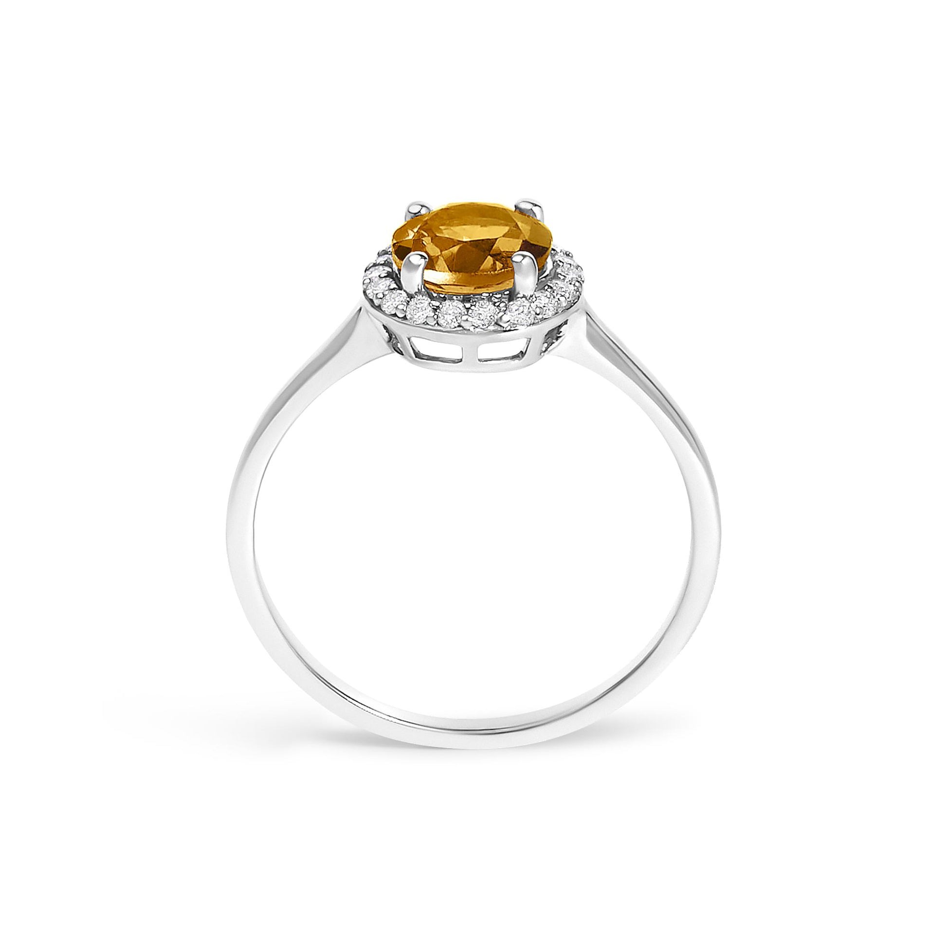 White metal ring viewed from the side, featuring a round orange gemstone in four-prong setting surrounded by a halo of round white gemstones in shared prong setting.