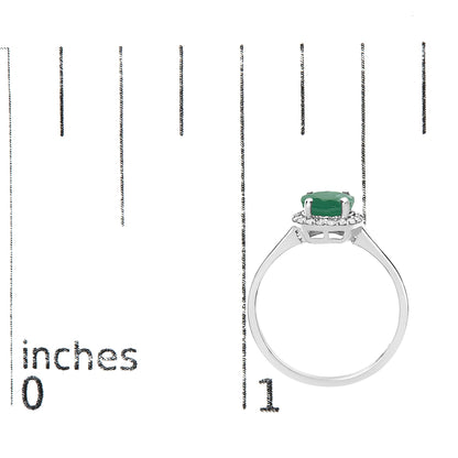 White metal ring with a round green gemstone in a four-prong setting, surrounded by multiple small white gemstones in a shared prong setting, shown on a scale from a side angle.