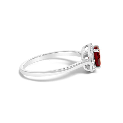 Side angle of a white metal ring with a central red round gemstone in a four-prong setting, surrounded by small round white gemstones in a shared prong setting.