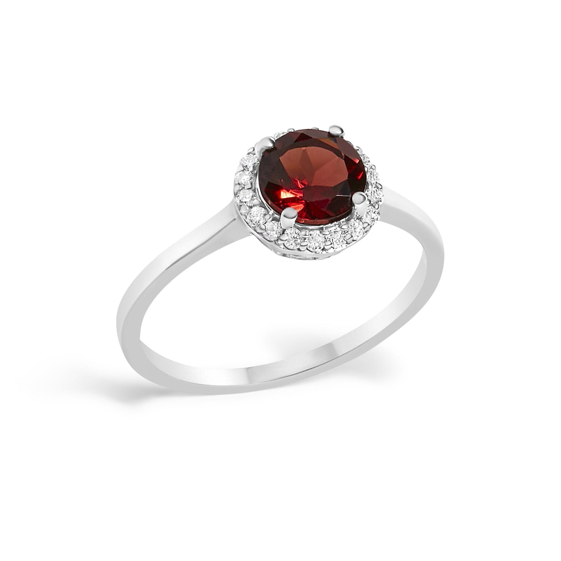 White metal ring with a round red gemstone center set in a four-prong setting, surrounded by a halo of round white gemstones in a shared prong setting, shown at a slight angle.