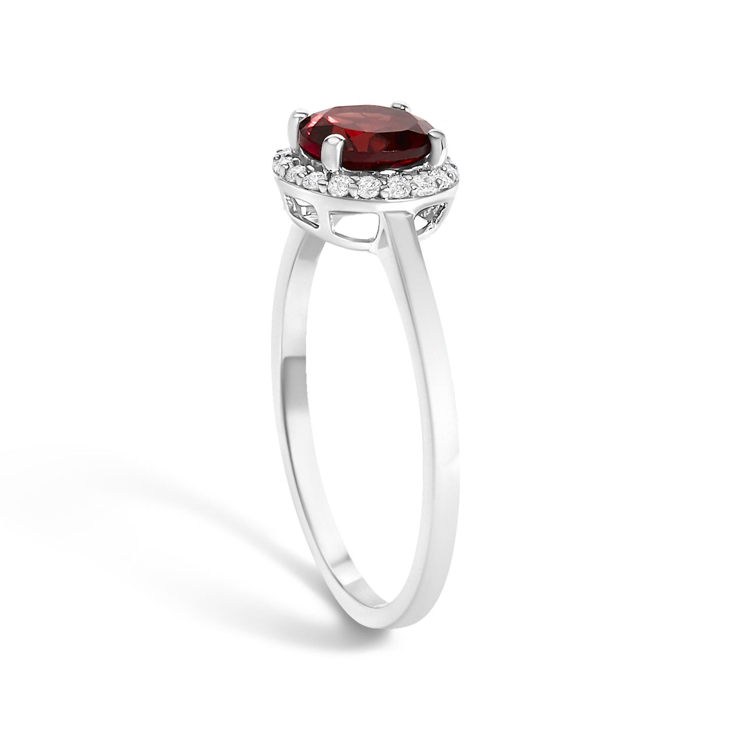 White metal ring with a round red gemstone held by four prongs, surrounded by a circle of small round white gemstones in shared prong setting, shown from a side angle.